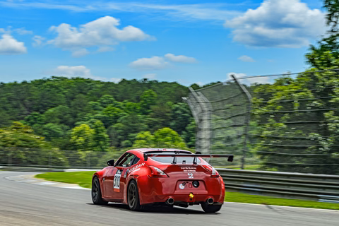 Plan Z Motorsports' red 2011 Nissan 370Z cornering hard on track